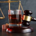 The concept of a DUI. Law hammer, alcohol and car keys on wooden table, dark background